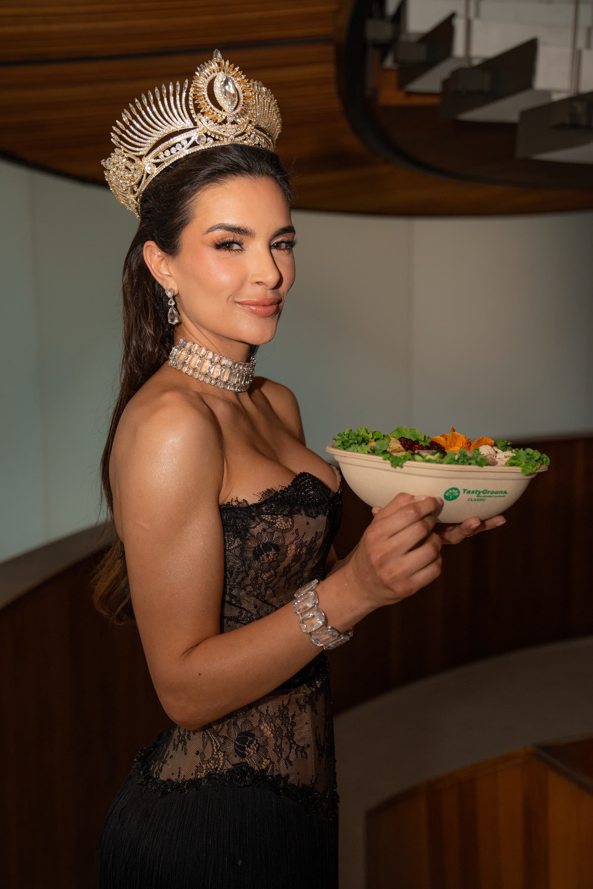 Reina de Miss Universe con corona y vestido de gala sosteniendo una ensalada Tasty Greens