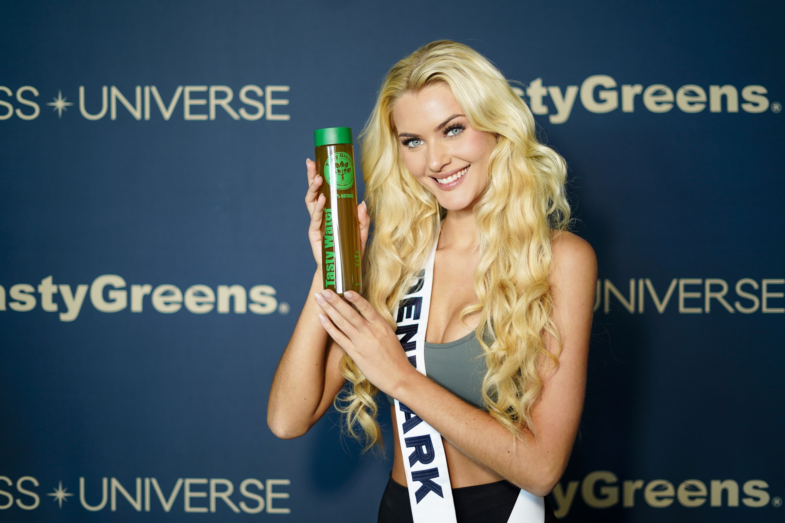 Miss Universe Dinamarca sosteniendo un jugo verde Tasty Greens