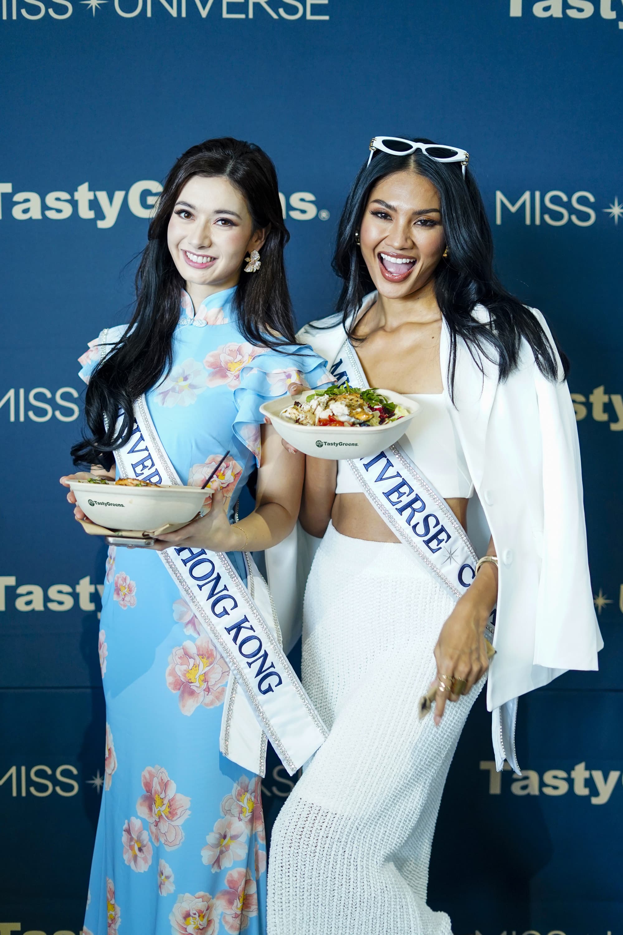 Candidatas de Hong Kong y Colombia con ensaladas Tasty Greens frente al backdrop Miss Universe